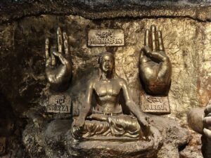 Golden sculpture of Indian mudras and a meditating figure on an ancient stone wall.