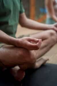 Close-up of a person sitting cross-legged in meditation on a yoga mat indoors.